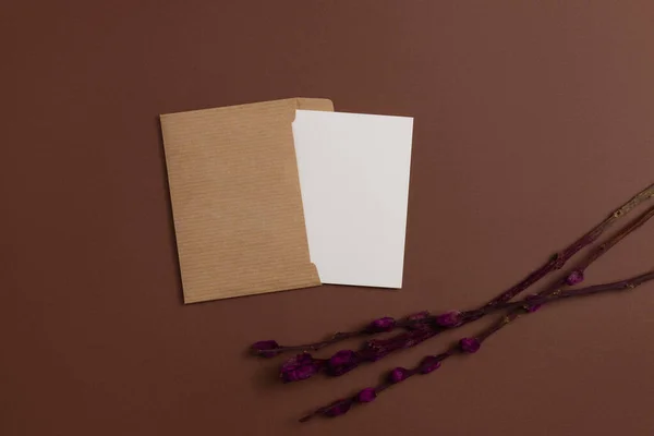 Mockup of a card made from eco-friendly materials and decorated with a composition of horizontally placed dried blooming branches dyed in red color on a brown background