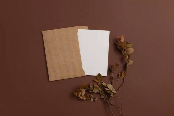 Mockup of an open card made of kraft paper and decorated with a composition of dried blueberry branches placed on a brown background