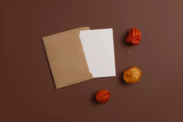 Mockup of an open card made from kraft paper and decorated with a composition of dried physalis flowers in orange color and placed on a brown background