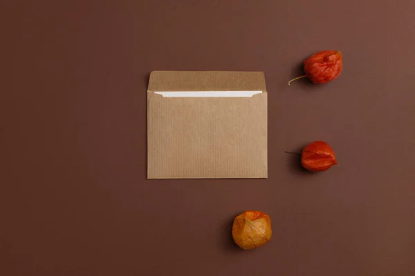 Mockup of a card made from craft paper and decorated with a composition of bright orange Physalis flowers placed on a brown background