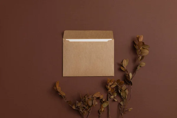 Mockup of a card made of kraft paper and decorated with a composition of dried blueberry twigs arranged on a brown background