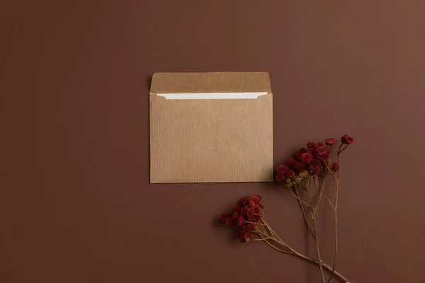 Mockup of a card made of kraft paper and decorated with a composition of dried flowers painted in bright red and arranged on a brown background