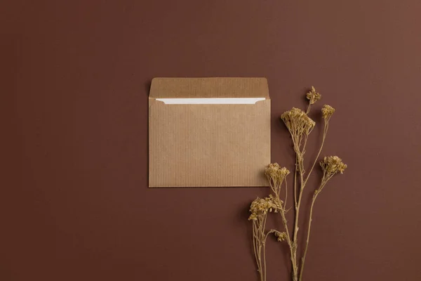 Mockup of a card made of eco-friendly kraft paper and decorated with a composition of dried meadow flowers arranged on a brown background
