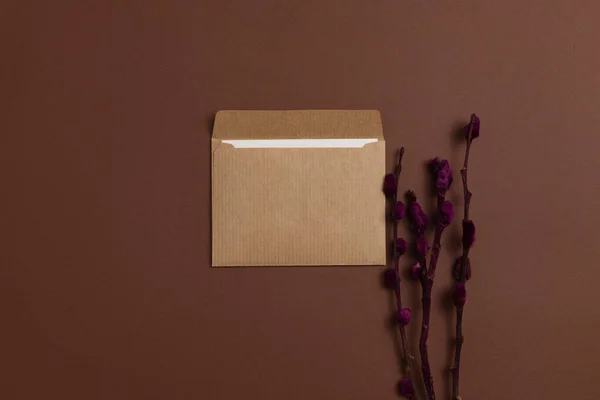 Mockup of a card made of eco-friendly kraft paper and decorated with a composition of dried blooming branches painted in burgundy color, placed on a brown background