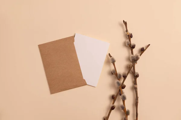 Mockup of an open invitation card made of eco-friendly kraft paper and decorated with a composition of dry flowering branches placed on a beige background