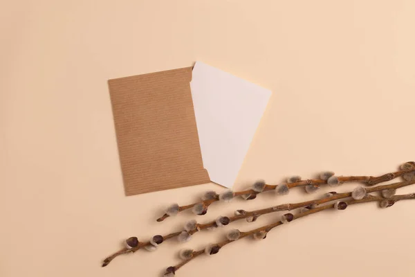 Mockup of an open invitation card made from eco-friendly craft paper and decorated with a composition of dry flowering branches placed horizontally on a beige background