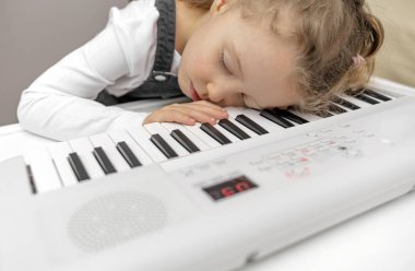 The child was tired of playing the synthesizer and fell asleep on the keys.