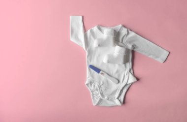 Çocuk kıyafetlerinin arka planında pozitif hamilelik testi var. Metin için boşluk var.