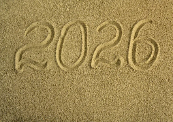 The date 2026 is written on the sea sand. Festive background.