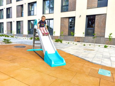 Neşeli bir kız bir çocuk kaydırağından iner.