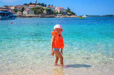 Can yeleği giymiş bir çocuk denizde duruyor..