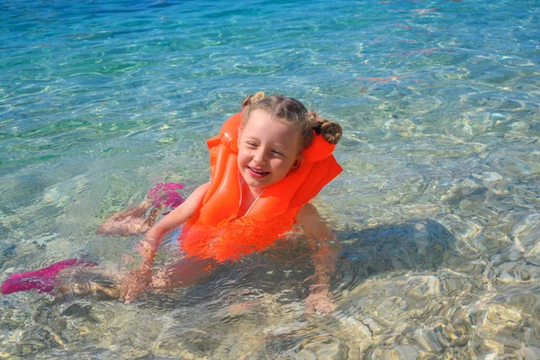 The child learns to swim in the sea in a bright life jacket.