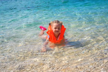 Çocuk parlak bir can yeleğiyle denizde yüzmeyi öğreniyor..