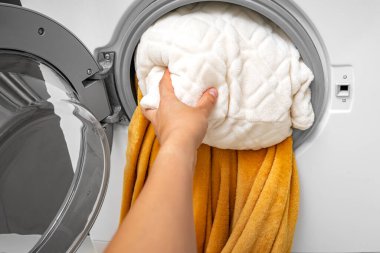 A hand pushes a pillow into the washing machine. Washing large items. clipart
