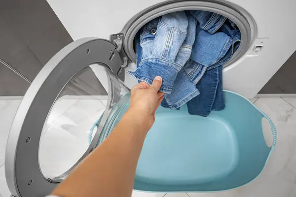 A hand takes out clean denim items from the washing machine.