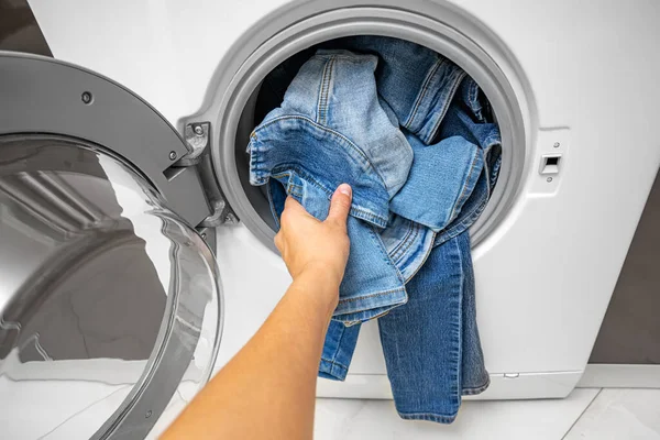 A hand takes out clean denim items from the washing machine.
