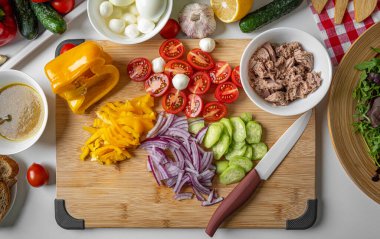 Salata için dilimlenmiş taze sebzeler tahta bir tahtanın üzerinde yatıyor..