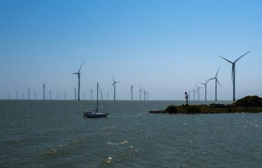 Mavi gökyüzünde bir sürü yel değirmeni türbini ve yat. Hollanda 'da. Kuzey Denizi.