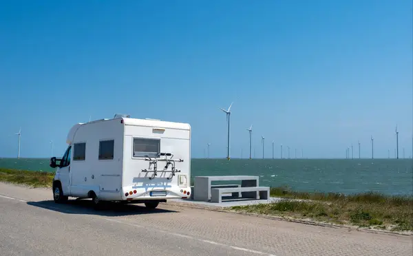 White Trailer on the road and Windmill in North sea on the blue sky background. Netherlands camp trip.