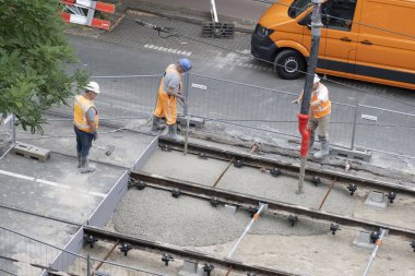 Laan van Nieuwe Oost-Indie, Lahey, Hollanda - 20 Ağustos 2024; Turuncu tulumlu çok sayıda yol işçisi tramvay raylarını onarıp yeni beton döker