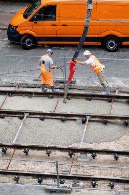 Laan van Nieuwe Oost-Indie, Lahey, Hollanda - 20 Ağustos 2024; Turuncu tulumlu çok sayıda yol işçisi tramvay raylarını onarıp yeni beton döker