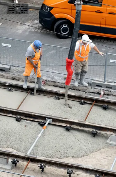 Laan van Nieuwe Oost-Indie, Lahey, Hollanda - 20 Ağustos 2024; Turuncu tulumlu çok sayıda yol işçisi tramvay raylarını onarıp yeni beton döker