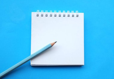 yakın ve düz bir kalem yatıyordu beyaz spiralli not defteri üzerinde bir masa mavi arka plan. Eğitim ve iş konsepti. Okul malzemeleri ve ofis işleri.