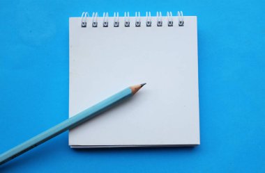 yakın ve düz bir kalem yatıyordu beyaz spiralli not defteri üzerinde bir masa mavi arka plan. Eğitim ve iş konsepti. Okul malzemeleri ve ofis işleri.