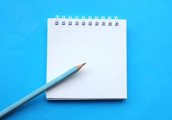 yakın ve düz bir kalem yatıyordu beyaz spiralli not defteri üzerinde bir masa mavi arka plan. Eğitim ve iş konsepti. Okul malzemeleri ve ofis işleri.