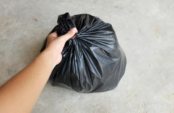 woman hands holding black garbage bags isolated on the cement floor background.symbol of waste management and environmental
