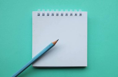 Masa yeşil pastel arka planda beyaz spiral bir not defterine bir kalem yerleştirin. Eğitim ve iş konsepti. Okul malzemeleri ve ofis işleri.
