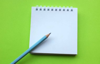 Yaklaş ve düz bir kalemle yeşil masa arkaplanına beyaz spiral bir not defteri koy. Eğitim ve iş konsepti. Okul malzemeleri ve ofis işleri.