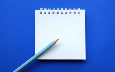 yakın ve düz bir kalem yatıyordu beyaz spiralli not defteri üzerinde bir masa mavi arka plan. Eğitim ve iş konsepti. Okul malzemeleri ve ofis işleri.