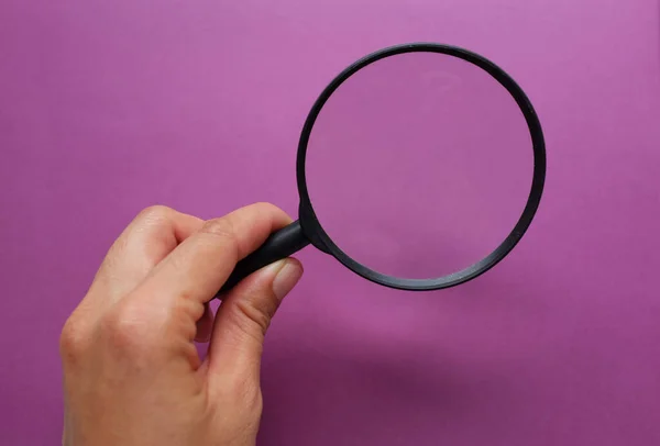 女人的手拿着一个黑色的框架 一个矩形彩色纸白色和紫色背景的放大镜 — 图库照片