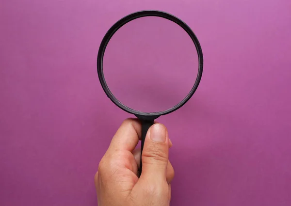 女人的手拿着一个黑色的框架 一个矩形彩色纸白色和紫色背景的放大镜 — 图库照片