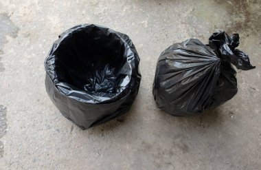 Beton zemine izole edilmiş siyah plastik torbalı çöp tenekesi. Atık yönetimi ve çevre sembolü.