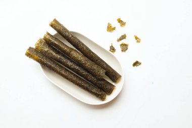 Çıtır yosun rulo atıştırmalıkları, bol yağda kızartılmış yosun ruloları, pişmiş, kurutulmuş, beyaz bir tepside beyaz bir tabağa konmuş. Atıştırmalıklar veya sağlıklı yiyecekler.