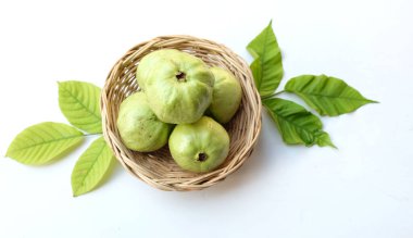 Üst görünümü taze yeşil bir guava (psidyum guajava linn) parlak yeşil kabuklu ve beyaz hamurlu, tatlı, çıtır çıtır bambu bir sepetin içinde beyaz bir arka planda izole edilmiş.