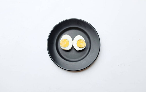 Аппетитные варёные яйца, разрезанные пополам на чёрной керамической тарелке.