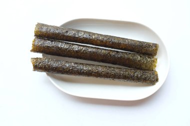 Çıtır yosun rulo atıştırmalıkları, bol yağda kızartılmış yosun ruloları, pişmiş, kurutulmuş, beyaz bir tepside beyaz bir tabağa konmuş. Atıştırmalıklar veya sağlıklı yiyecekler.