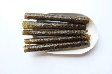 Çıtır yosun rulo atıştırmalıkları, bol yağda kızartılmış yosun ruloları, pişmiş, kurutulmuş, beyaz bir tepside beyaz bir tabağa konmuş. Atıştırmalıklar veya sağlıklı yiyecekler.