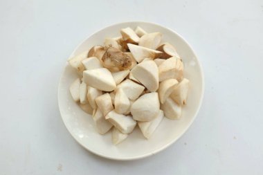 Üst ve düz bir beyaz arka planda izole edilmiş beyaz bir tabakta çiğ çiğ kral istiridye mantarları ve rosmary (Pleurotus eryngii) yatar.