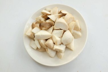 Üst ve düz bir beyaz arka planda izole edilmiş beyaz bir tabakta çiğ çiğ kral istiridye mantarları ve rosmary (Pleurotus eryngii) yatar.