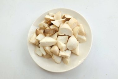 Üst ve düz bir beyaz arka planda izole edilmiş beyaz bir tabakta çiğ çiğ kral istiridye mantarları ve rosmary (Pleurotus eryngii) yatar.