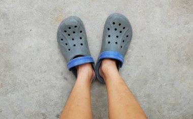 Bacaklı kadın ve çimentoda izole edilmiş bir çift mavi takunya. Topuklu silikon kayışlı ve delikli yaz su ayakkabıları . 