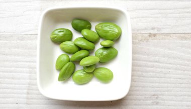 Acı fasulye, bükülmüş fasulye, kokuşmuş fasulye, Sato, Petai veya Pakria, (Parkia speciosa) ahşap masa üzerinde beyaz kase içinde. Tayland ve Asya İçindekiler için bitkiler. Tayland 'ın güneyinde en sevilen yiyecek.