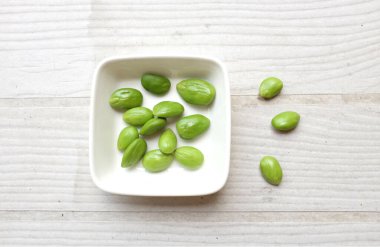 Acı fasulye, bükülmüş fasulye, kokuşmuş fasulye, Sato, Petai veya Pakria, (Parkia speciosa) ahşap masa üzerinde beyaz kase içinde. Tayland ve Asya İçindekiler için bitkiler. Tayland 'ın güneyinde en sevilen yiyecek.