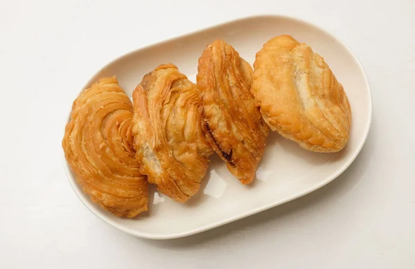 deep fried curry puff,curry puff pastry, karipap,epok epok, spiral curry puff in a white ceramic plate isolated a white backdrop  . thai curry puff concept.this pastry is asian traditional snacks