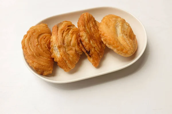 deep fried curry puff,curry puff pastry, karipap,epok epok, spiral curry puff in a white ceramic plate isolated a white backdrop  . thai curry puff concept.this pastry is asian traditional snacks