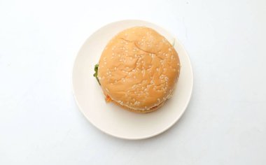 Domuz pirzolası ve domatesli klasik burger. Salatalık, kırmızı soğan, peynir ve marullu susamlı çörek. Beyaz bir arka planda izole edilmiş beyaz plaka üzerinde. Amerikan hamburgeri